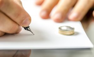 Hand signing a document with a fountain pen beside a wedding ring