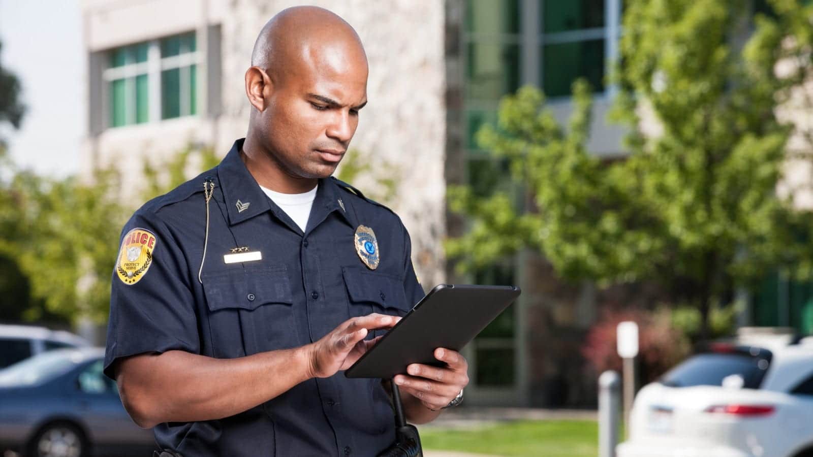 Police officer entering information on a tablet outside a building