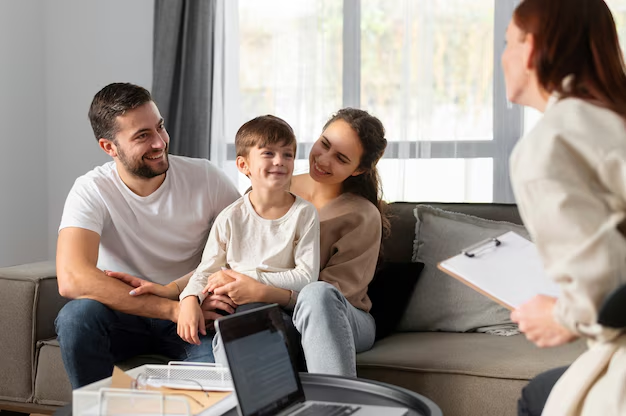 Parents and a young boy on a sofa talking with a counselor holding a clipboard