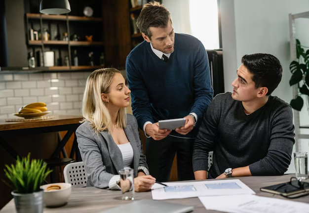 Advisor showing a tablet to a young couple reviewing paperwork at a table