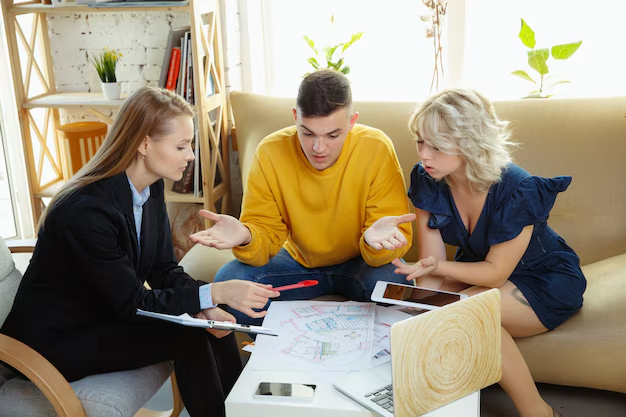 Couple gesturing in disagreement while a woman reviews house plans with them