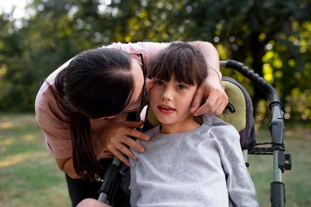 Woman leaning in to comfort a girl seated in a wheelchair outdoors