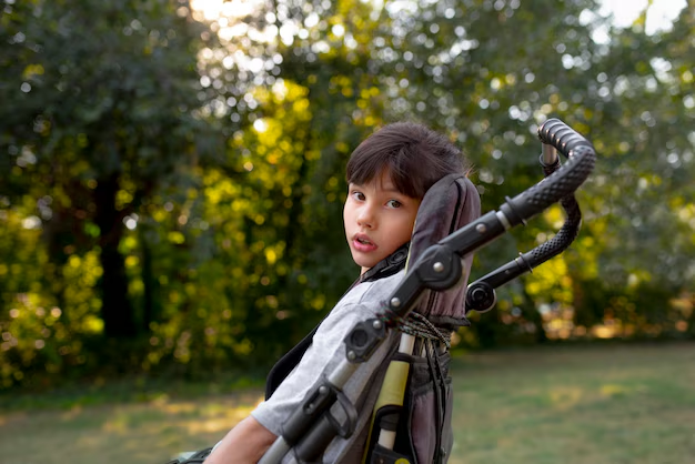 Young child seated in a wheelchair outdoors in front of trees