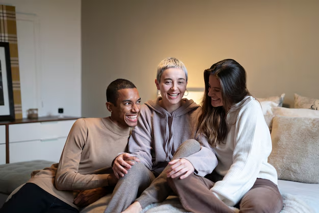 Three young adults laughing together on a bed