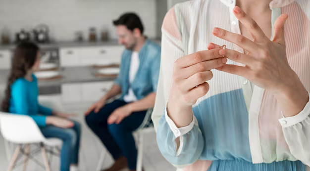 Woman removing her wedding ring with a man and child blurred in the background