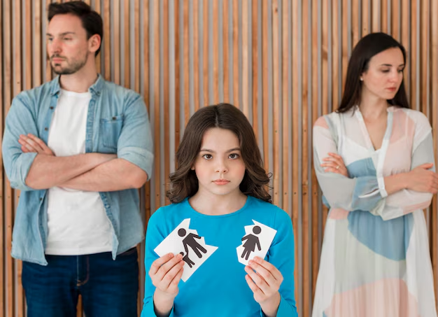 Girl holding a torn paper family cutout while her parents stand apart behind her