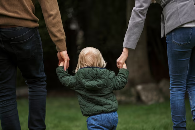 Two adults walking across a lawn holding a toddler's hands