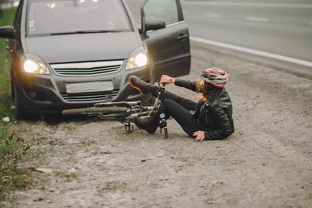 Cyclist in a helmet sitting on the road beside a fallen bike and a car