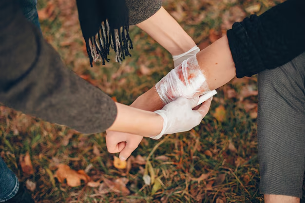 Gloved hands bandaging an injured arm outdoors on fallen leaves
