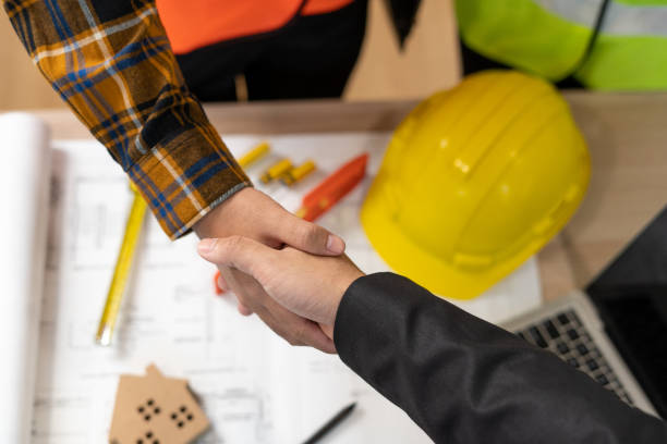 Handshake over building blueprints next to a yellow hard hat