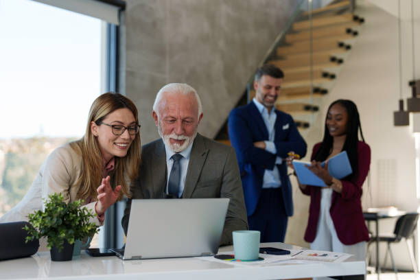 Older man and young woman looking at a laptop while two colleagues talk behind them