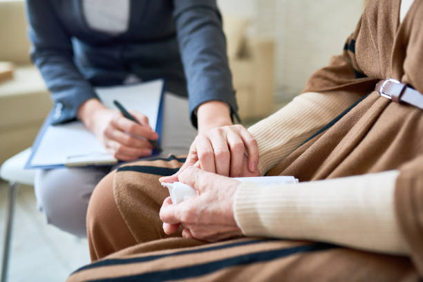 Counselor with a clipboard holding the hand of an older woman clutching a tissue