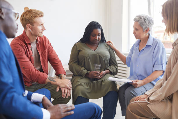 Support group seated in a circle, an older woman comforting a woman holding a glass of water