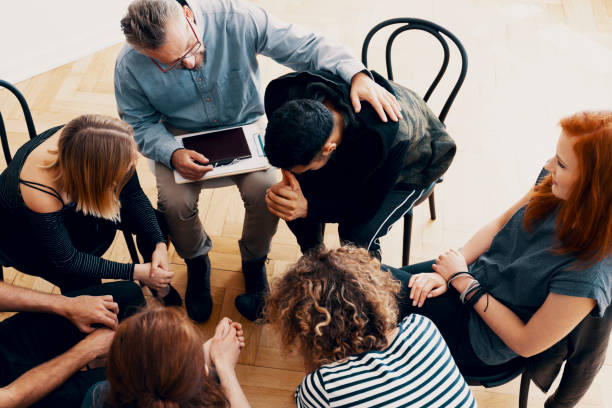 Group counseling session with a therapist comforting a man in a circle of chairs