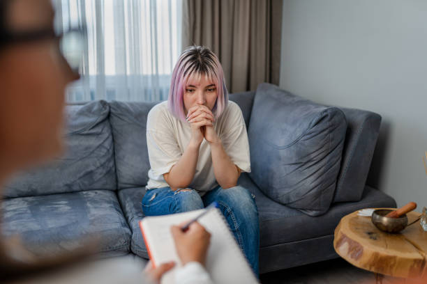 Young woman sitting on a couch with clasped hands while a counselor takes notes