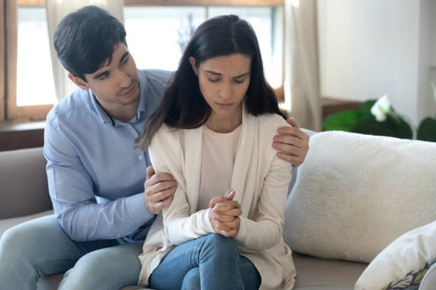 Man comforting a sad woman with his hands on her shoulders on a sofa
