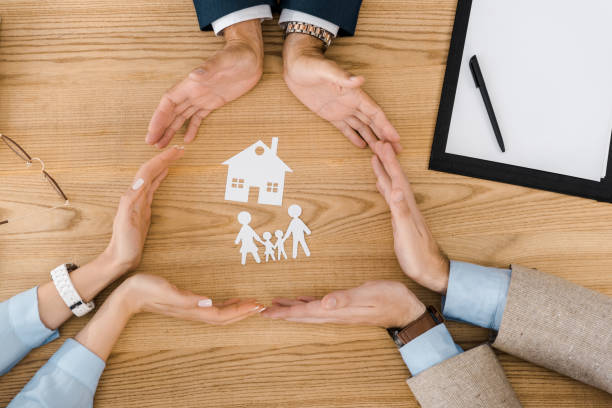 Hands encircling paper cutouts of a house and family on a wooden table