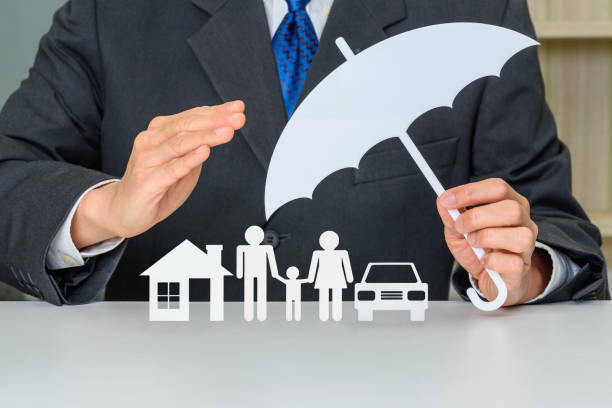 Man in a suit holding a paper umbrella over paper cutouts of a house, family and car
