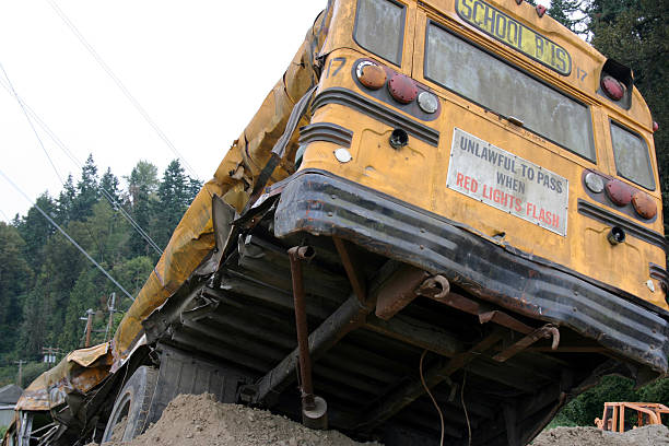 Wrecked yellow school bus tilted on a dirt mound with its rear end crushed