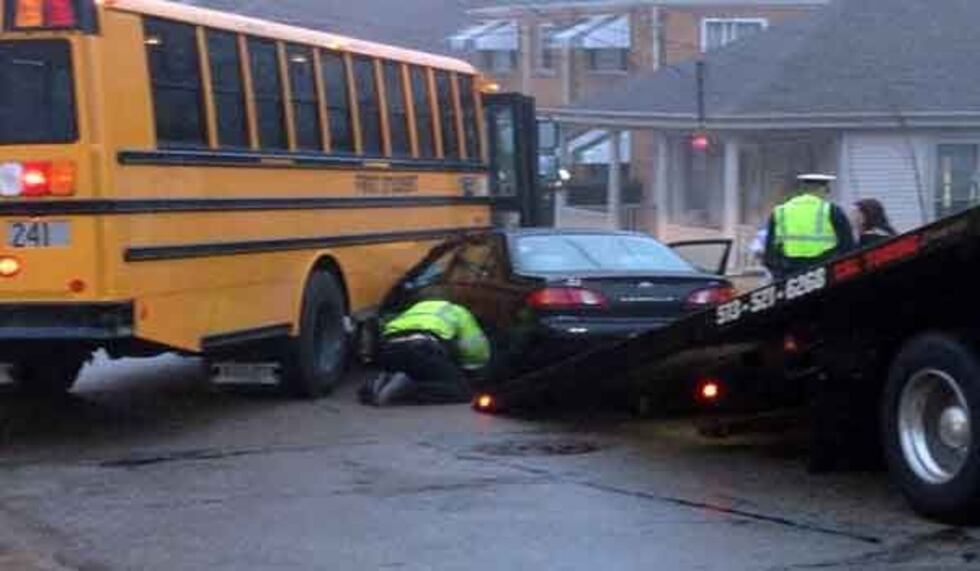 Yellow school bus stopped beside a crashed black car being loaded onto a tow truck