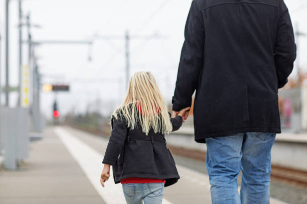 Young girl holding an adult's hand while walking along a train platform
