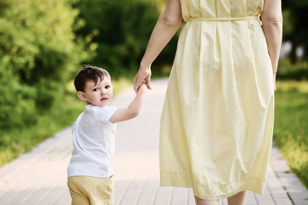 Toddler looking back while holding a woman's hand on a park path