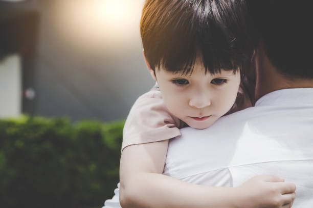 Sad young child resting on an adult's shoulder outdoors