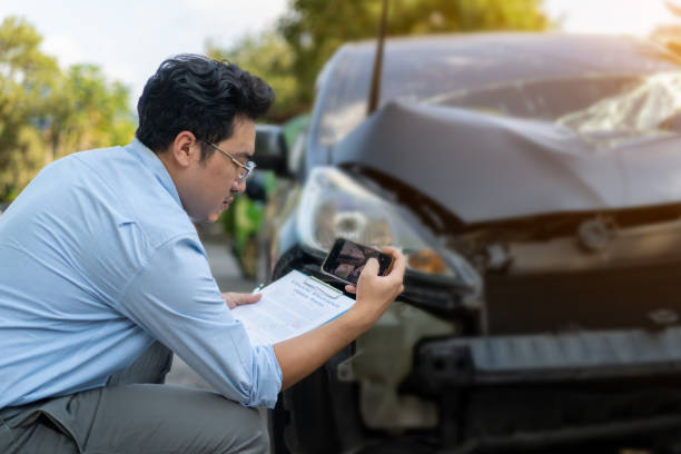 Man photographing a damaged car with a phone while filling out a form