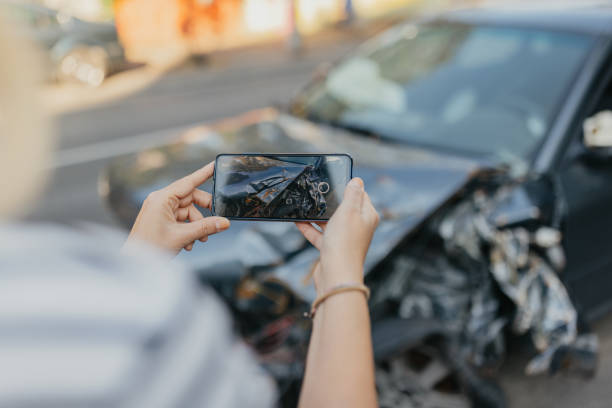 Person photographing a crashed car's front-end damage with a phone