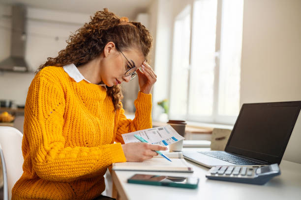 Young woman at a desk holding her head while reading a bill