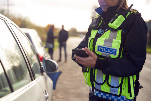Police officer in a hi-vis vest writing on a phone beside a car at a roadside