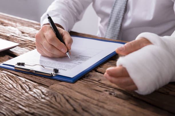 Person with a bandaged arm filling out an insurance claim form on a clipboard