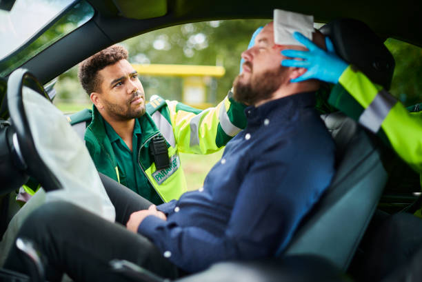 Paramedic pressing a gauze pad to an injured driver's forehead inside a car