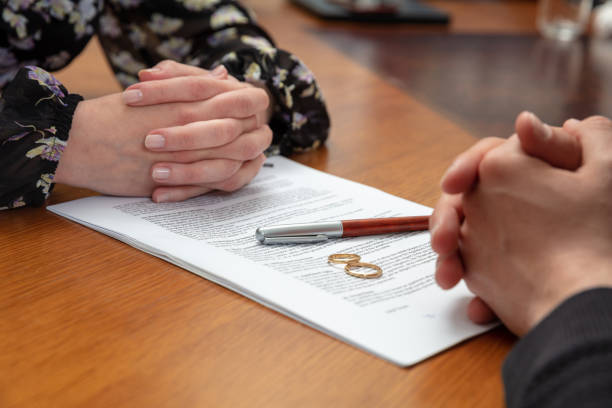 Two people's clasped hands on either side of a contract with a pen and two rings