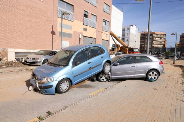 Damaged blue car resting on top of a silver car on a city street