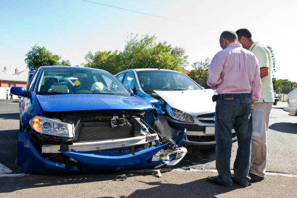 Two men inspecting a blue car with a crushed front end after a collision
