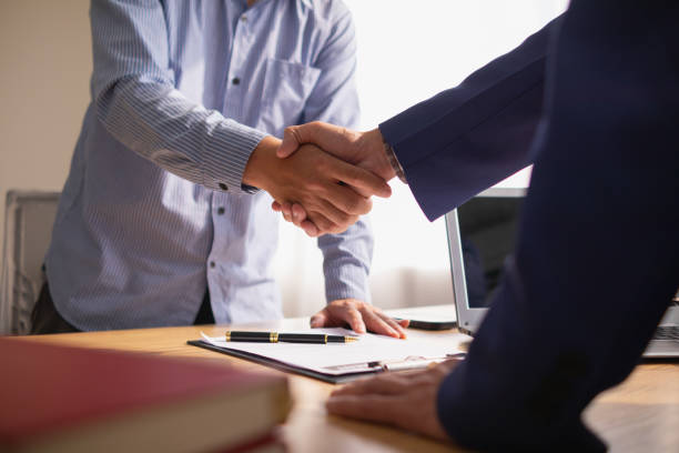 Two people shaking hands over a signed contract at a desk