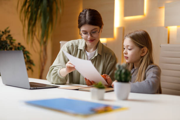 Woman reading a document at a desk beside a young girl