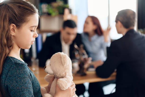 Sad girl holding a teddy bear while adults argue in the background