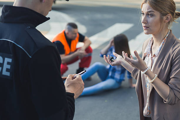Police officer taking a statement from a woman at an accident scene while a paramedic helps someone on the road