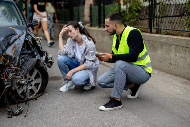 Man in a high-visibility vest crouching beside a distressed woman next to a wrecked car